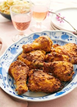 A platter of air fryer fried chicken with bubbly drinks, plates, and coleslaw in the background.