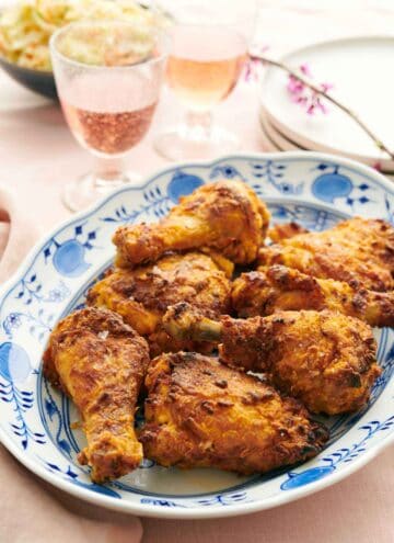 A platter of air fryer fried chicken with bubbly drinks, plates, and coleslaw in the background.