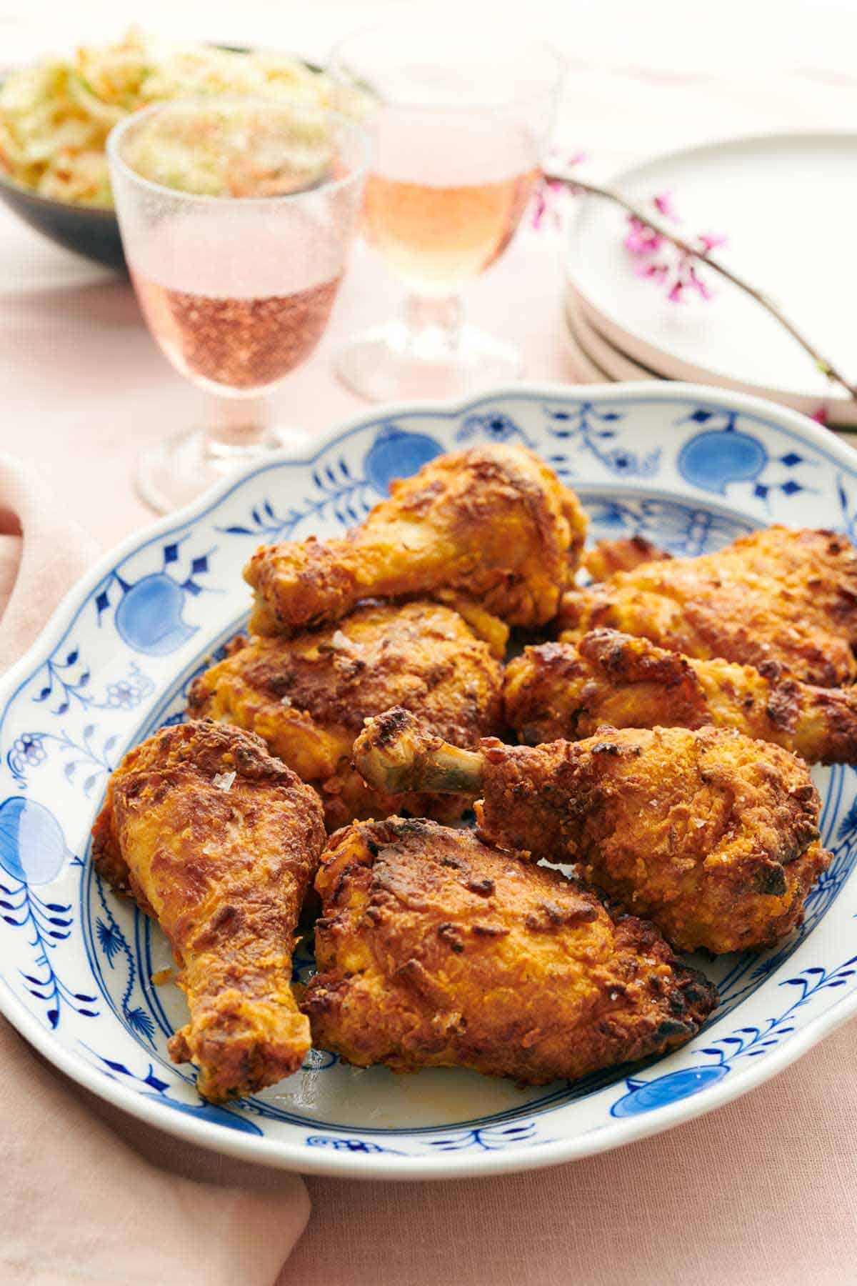 A platter of air fryer fried chicken with bubbly drinks, plates, and coleslaw in the background.