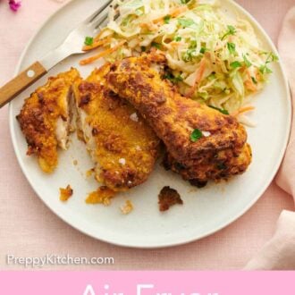 Pinterest graphic of a plate with two pieces of air fryer fried chicken with a piece cut along with coleslaw.