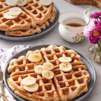 Pinterest graphic of a plate with a large banana waffle topped with syrup and sliced bananas. A stack of two waffles in the back along with syrup.