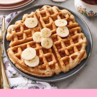 Pinterest graphic of a plate of banana waffle topped with sliced bananas with syrup, butter, plates, and forks in the back.