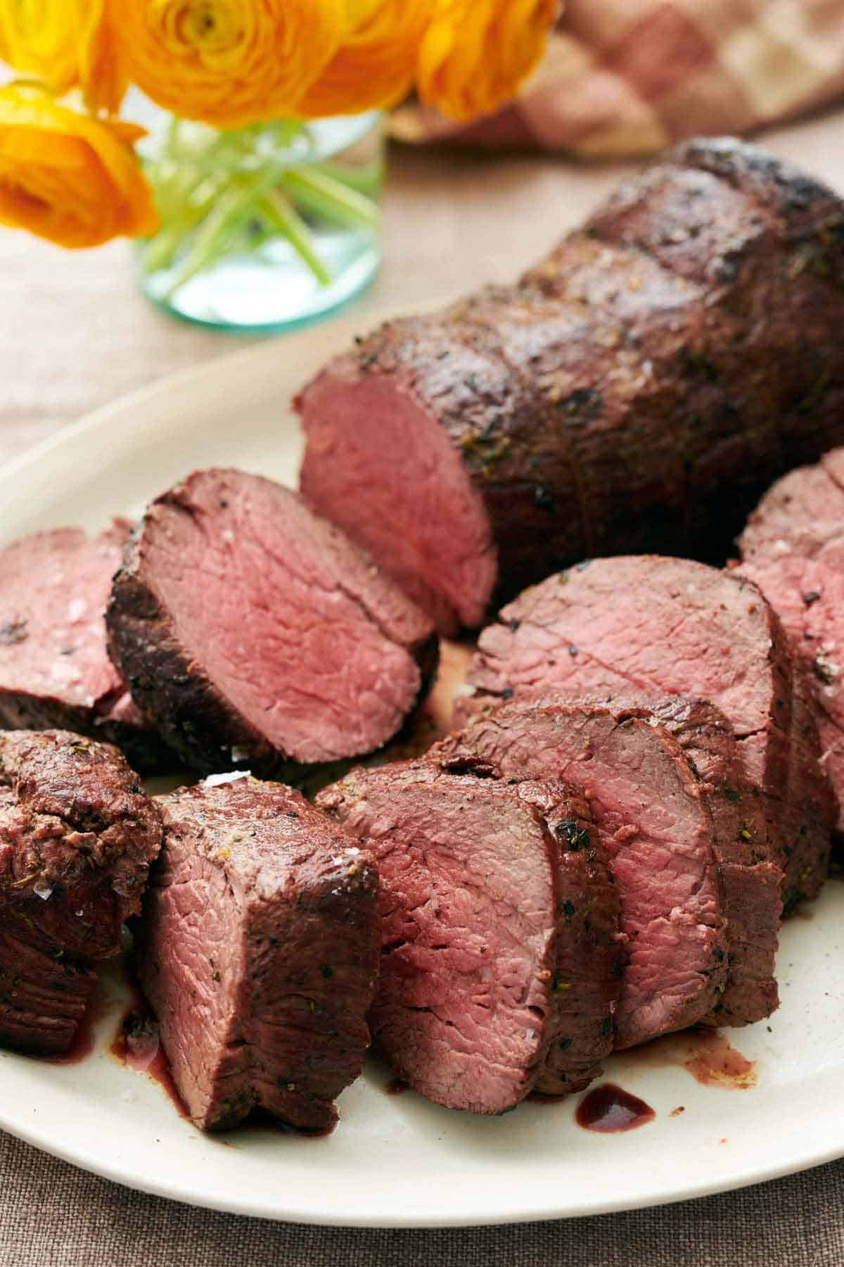 A close up view of sliced beef tenderloin on a platter. Flowers in the background.