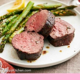 Pinterest graphic of a plate with three pieces of beef tenderloin with roasted asparagus and a lemon wedge.