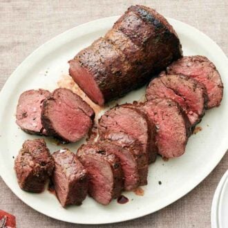 Overhead view of a platter with sliced beef tenderloin along with half not yet sliced. A napkin off to the side.