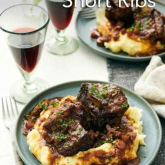 Pinterest graphic of a plate of mashed potatoes with braised beef short ribs on top. A second plate and two glasses of wine in the background.