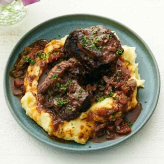 A plate of mashed potatoes with braised beef short ribs on top.