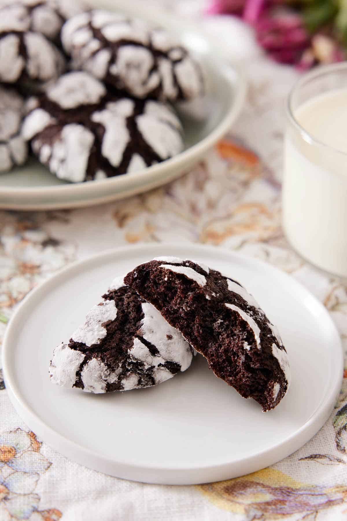 A plate with one chocolate crinkle cookie broken in half. One half stacked on the other, showing the cookie's interior.