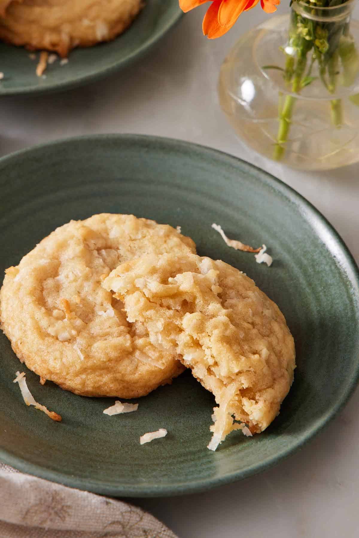 A green plate with a coconut cookie with a half eaten one leaning on it.