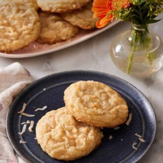 Pinterest graphic of a blue plate with two coconut cookies. Flowers and more cookies on a platter in the background.