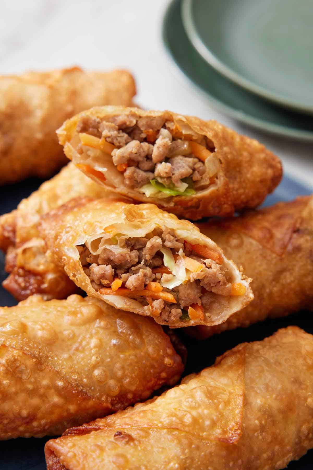 A stack of egg rolls with the ones on top, cut in half, showing the interior.