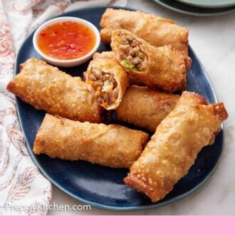 Pinterest graphic of a platter of egg rolls with one cut in half on top. A small bowl of dip in the platter and fried rice in the background.