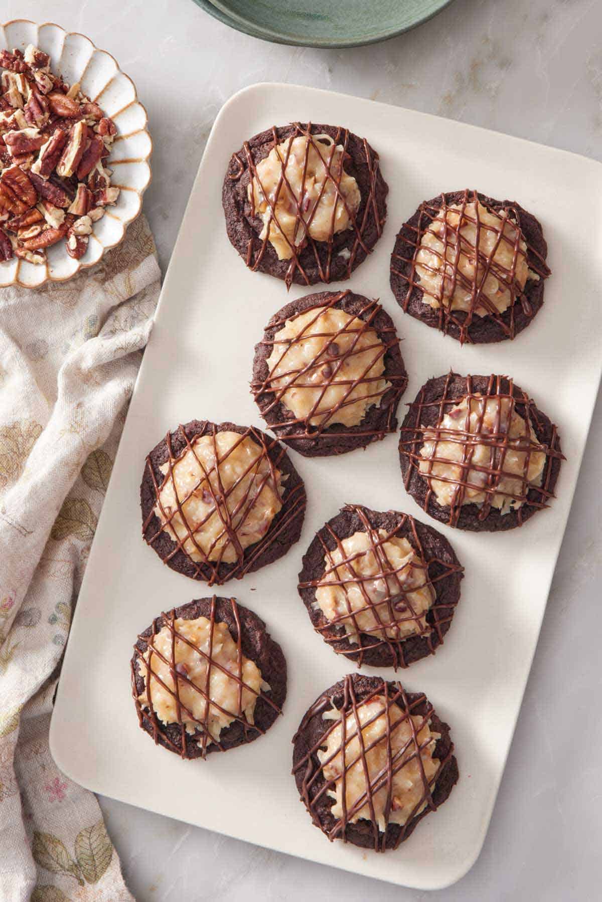 Overhead view of a platter of German chocolate cookies with a bowl of chopped pecans on the side.