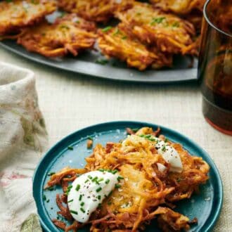 Pinterest graphic of a plate with two potato latkes topped with sour cream and chives. More on a platter in the background.