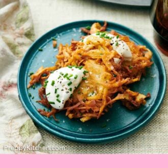 Pinterest graphic of a plate with two crispy potato latkes topped with sour cream, chives, and pepper.