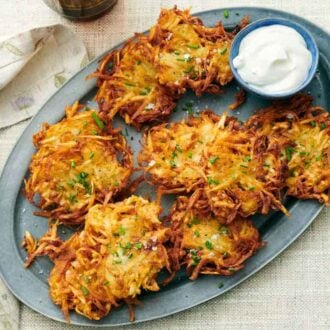 Overhead view of a platter of potato latkes with a bowl of sour cream.