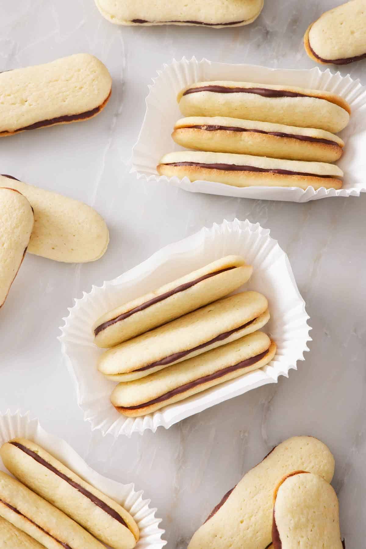 Overhead view of sets of three Milano cookies in paper holders. More Milano cookies scattered around.