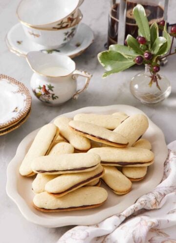 A platter of Milano cookies. Coffee, cream, and cups in the background along with some decorative plants.