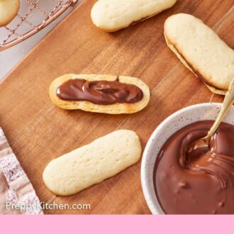 Pinterest graphic of a Milano cookie in the process of being assembled with melted chocolate spread onto a cookie.