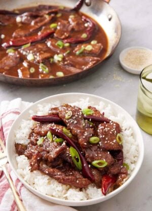 A plate of Mongolian beef over rice. A skillet of more Mongolian beef in the background.