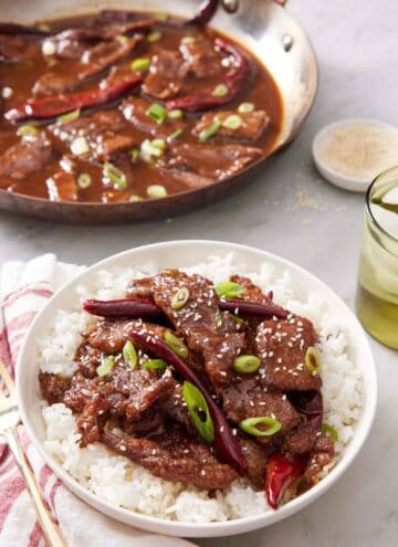 A plate of Mongolian beef over rice. A skillet of more Mongolian beef in the background.