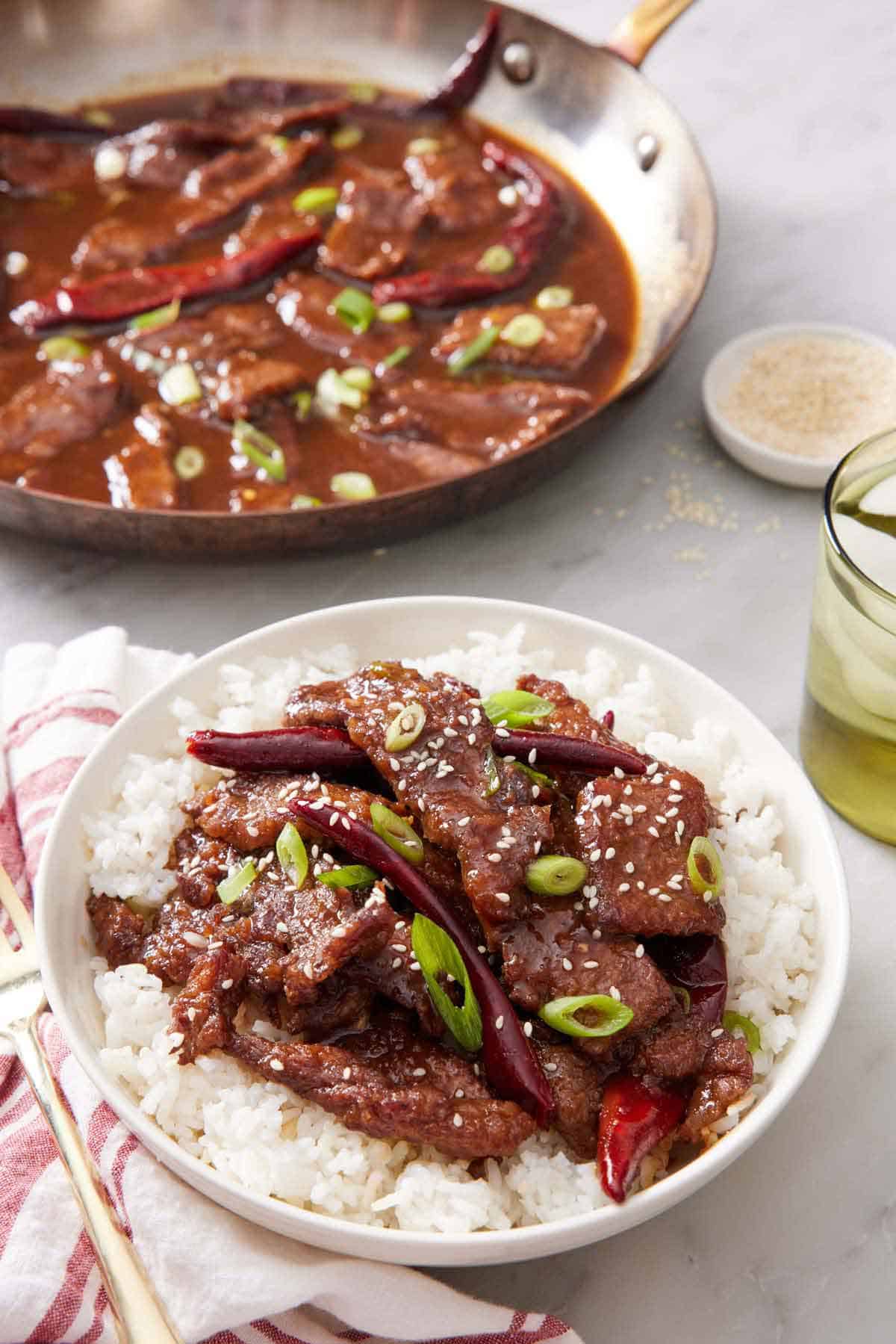 A plate of Mongolian beef over rice. A skillet of more Mongolian beef in the background.