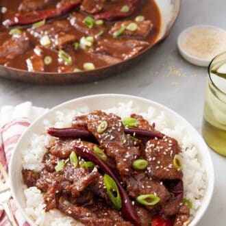 Pinterest graphic of a plate of Mongolian beef over rice. A skillet of more Mongolian beef in the background.