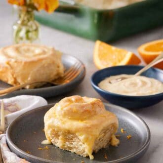 Pinterest graphic of a plate with an orange rolls. A bowl of glaze in the background also with another plated roll and a baking dish with the rest.