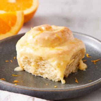 A plate with an orange roll with cut oranges in the background.