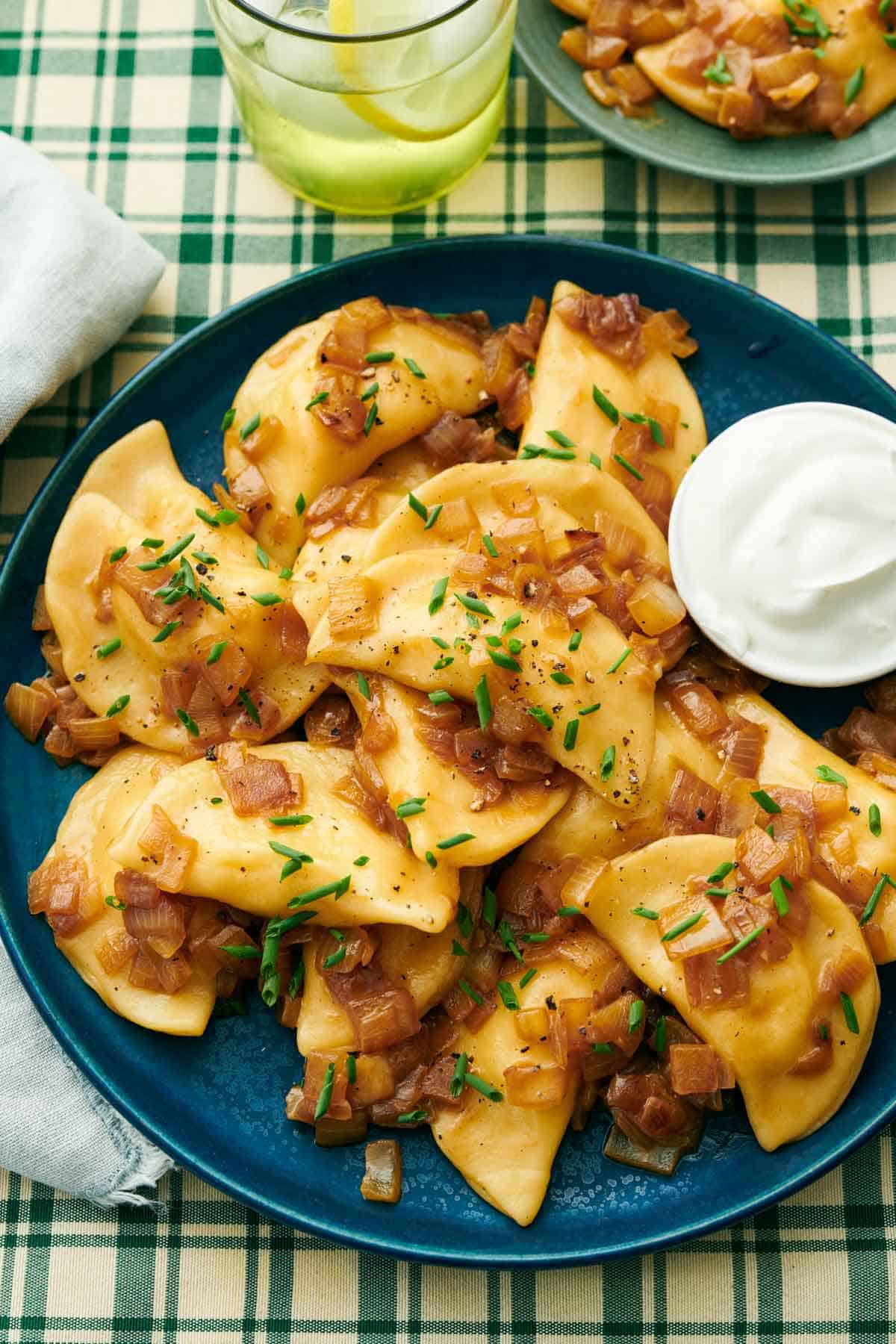 A platter of pierogies with a small bowl of sour cream on the side. Chives on top.