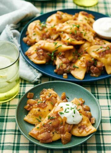 A plate with pierogies topped with sour cream and chives with a platter with more in the background.