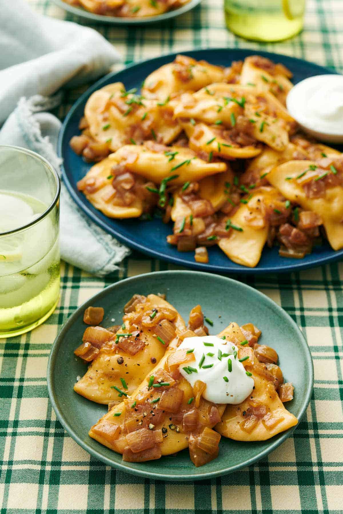 A plate with pierogies topped with sour cream and chives with a platter with more in the background.