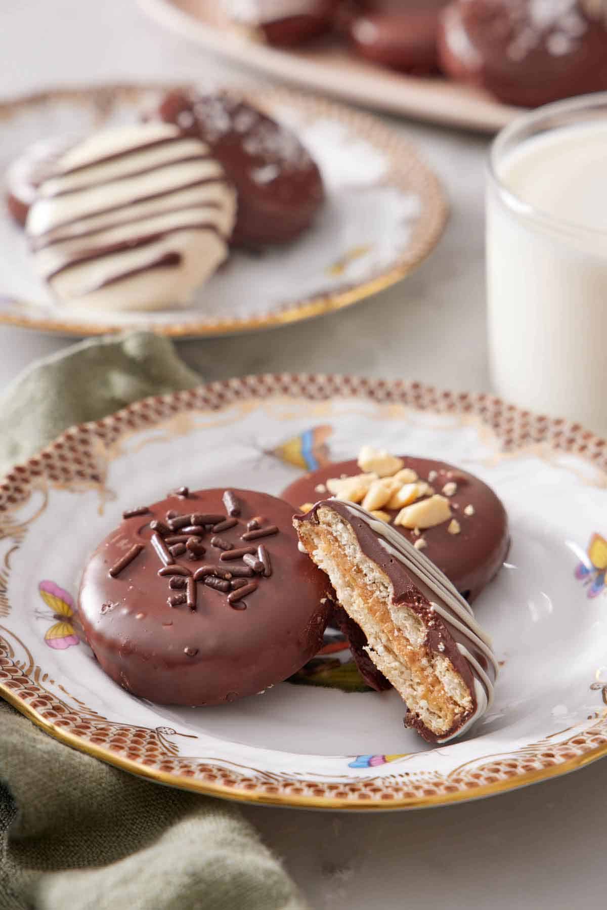 A plate with two Ritz cookies with a cut half leaning up. A glass of milk and more cookies in the background.