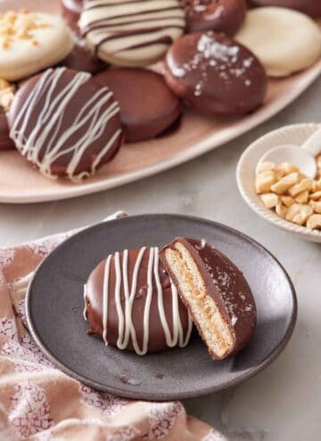 A plate with a Ritz cookie with a cut half leaning on top of it. A platter with more Ritz cookies with various toppings in the background.