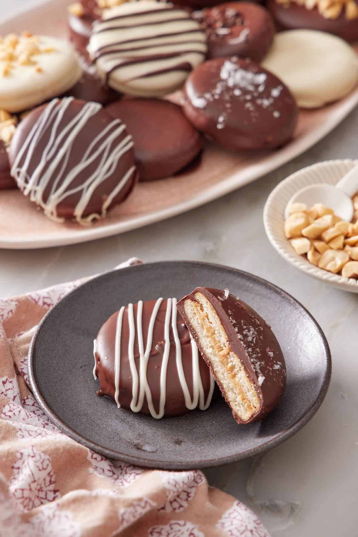 A plate with a Ritz cookie with a cut half leaning on top of it. A platter with more Ritz cookies with various toppings in the background.