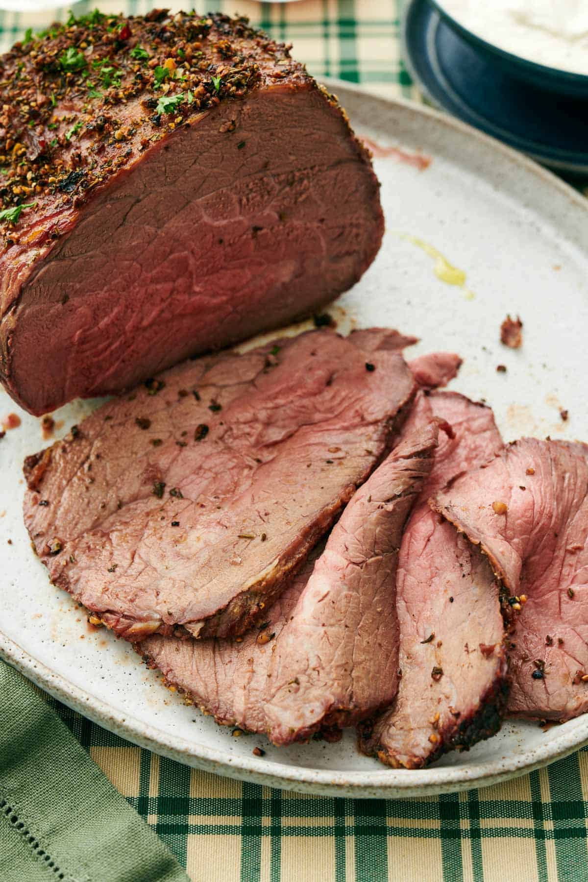 A close up view of the multiple thinly sliced slices of roast beef on a platter with half of the uncut roast.