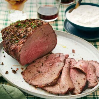 Pinterest graphic of a platter with a roast beef with half of it sliced in front. A bowl of sauce, drinks, and flowers in the back.