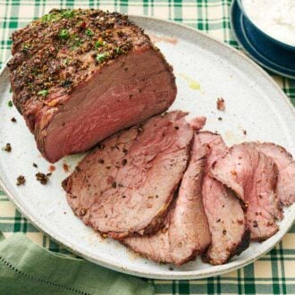 A platter of a partially sliced roast beef. Horseradish sauce in the back with a spoon.