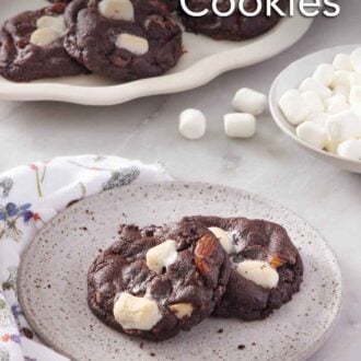 Pinterest graphic of a plate with two rocky road cookies and a platter more in the background. A bowl of mini marshmallows on the side.