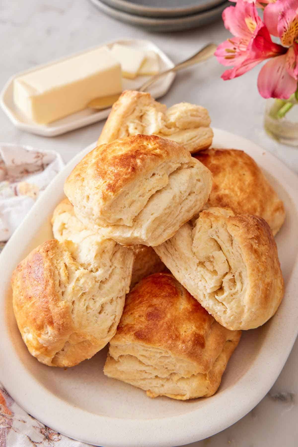 A white platter of sourdough biscuits with butter in the background.