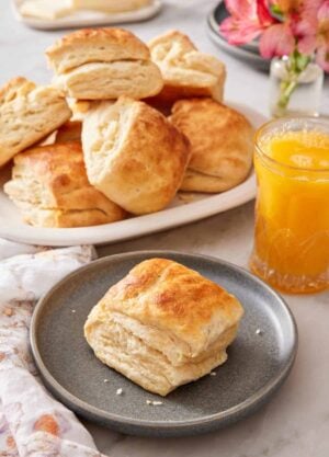 A plate with a sourdough biscuit with an orange juice and platter of more biscuits in the background.