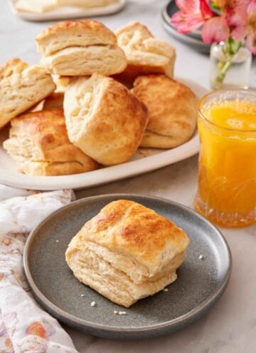 A plate with a sourdough biscuit with an orange juice and platter of more biscuits in the background.