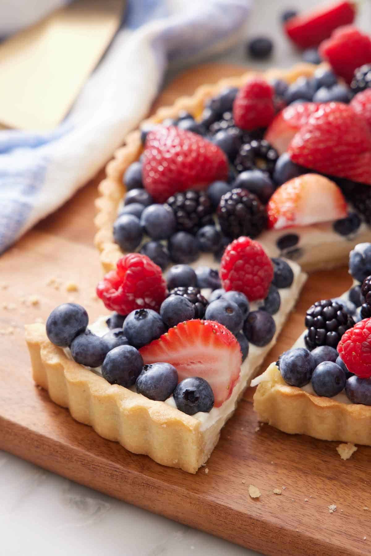 A slice of tart topped with fruit cut and pulled forward, showing the edge of the tart crust.