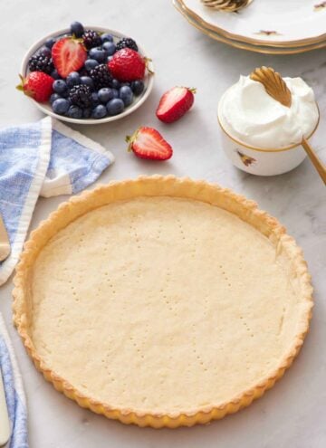 A baked tart crust with a bowl of berries and whipped cream in the background.