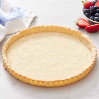 A baked tart crust with a bowl of assorted berries and a linen napkin in the background.