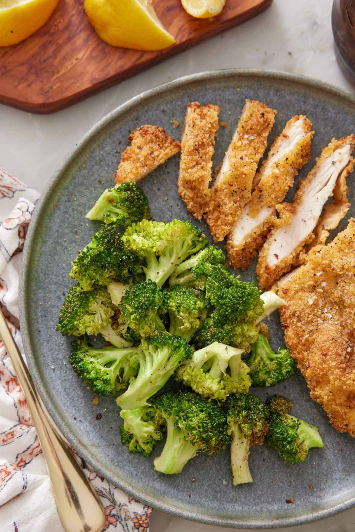 Overhead view of a plate of air fryer broccoli with a cut fried chicken cutlet.