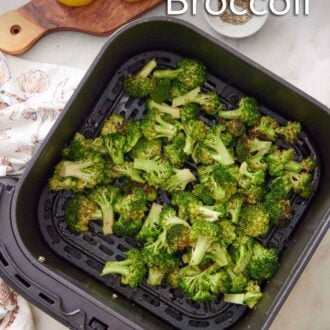 Pinterest graphic of broccoli in an air fryer basket. Cut lemon wedges, a bowl of pepper, and bowl of salt on the side.