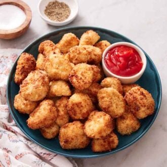 A plate of air fryer chicken nuggets with a small bowl of ketchup. Salt and pepper in the background.