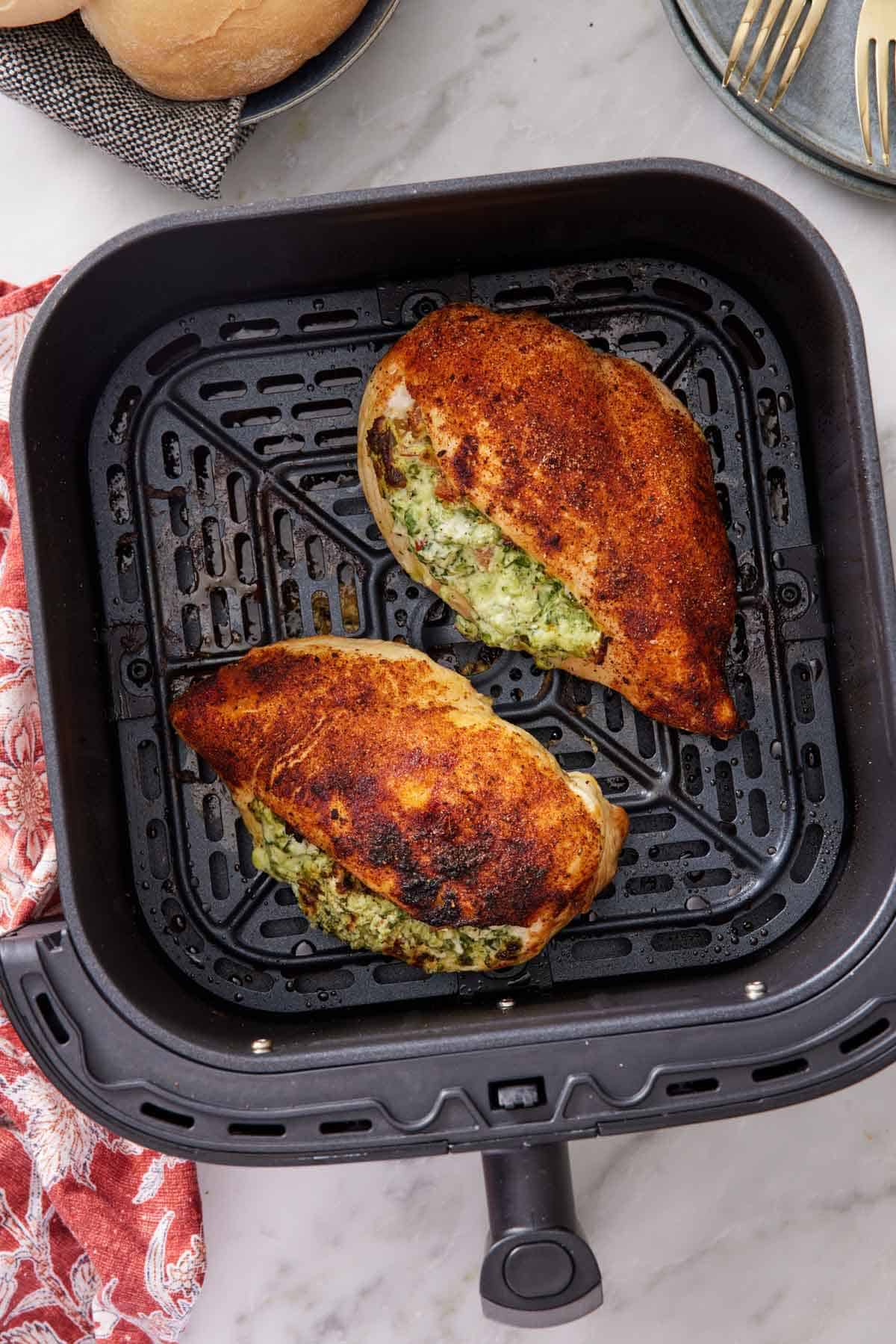 Overhead view of two air fryer stuffed chicken breasts in an air fryer basket.