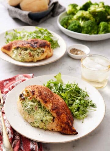 A plate with an air fryer stuffed chicken breast with some arugula. A drink, another plated serving, broccoli, and bread in the background.